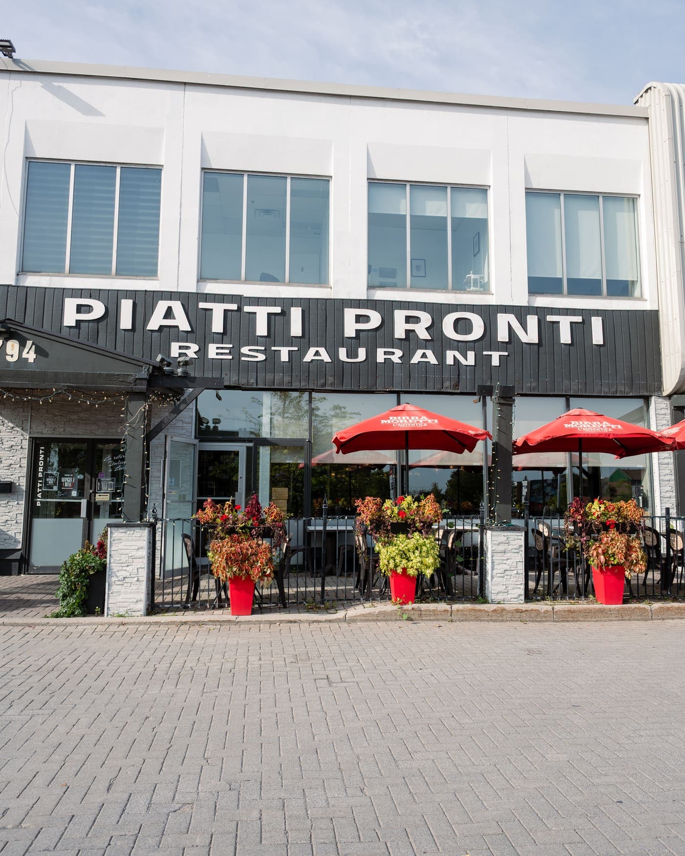 The Piatti Pronti storefront, its sign and its terrace with red umbrellas