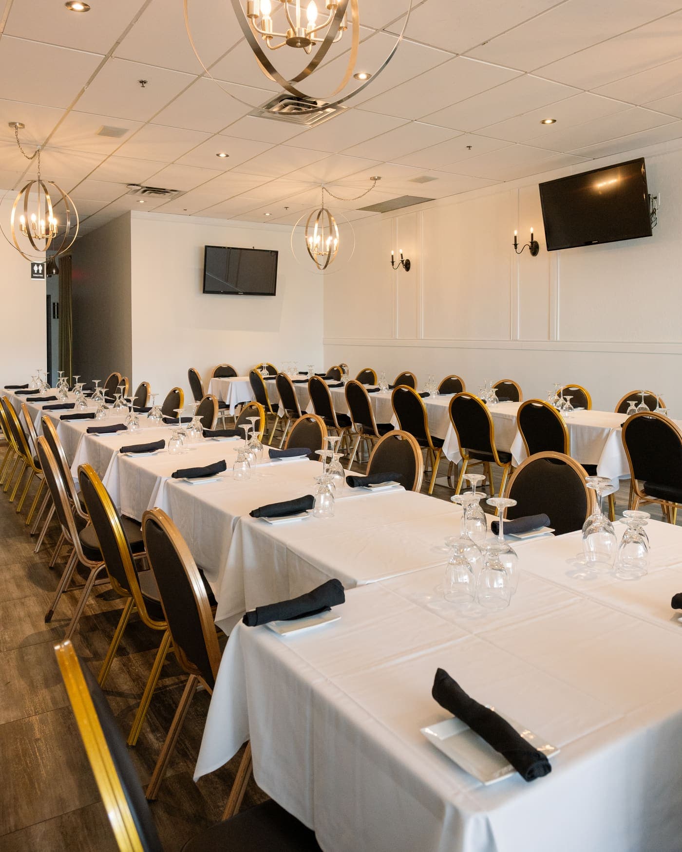The private room set for a group: long white-clothed tables under gold chandeliers