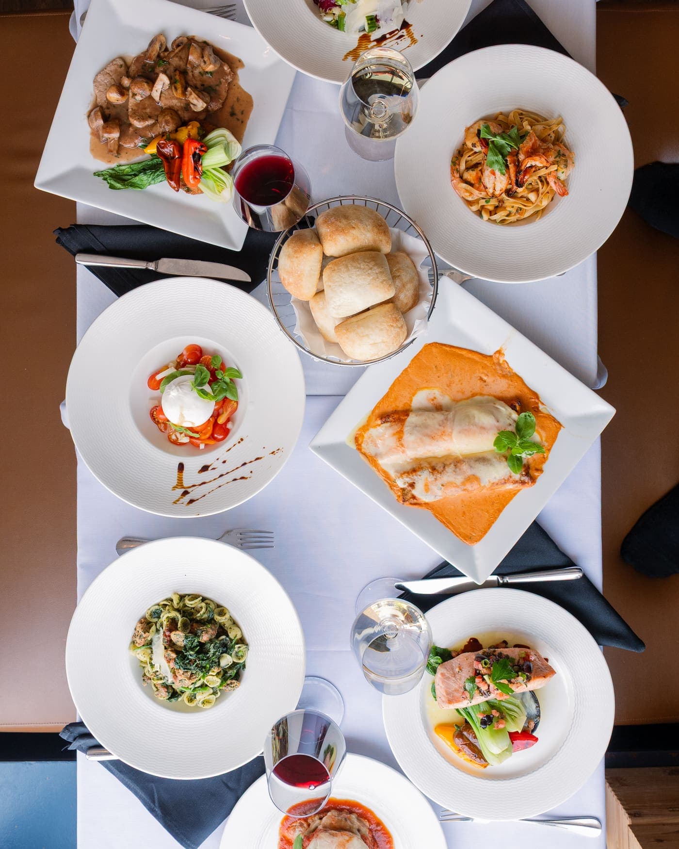 A table seen from above: burrata, shrimp fettuccine, baked cannelloni, orecchiette, salmon, bread and glasses of wine